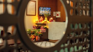 A room with a wooden reception desk, a TV screen, and a decorative altar with flowers and offerings.