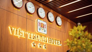 Zona de recepción de un hotel con relojes mostrando las horas de Tokio, Pekín, Hanói, París y Nueva York.