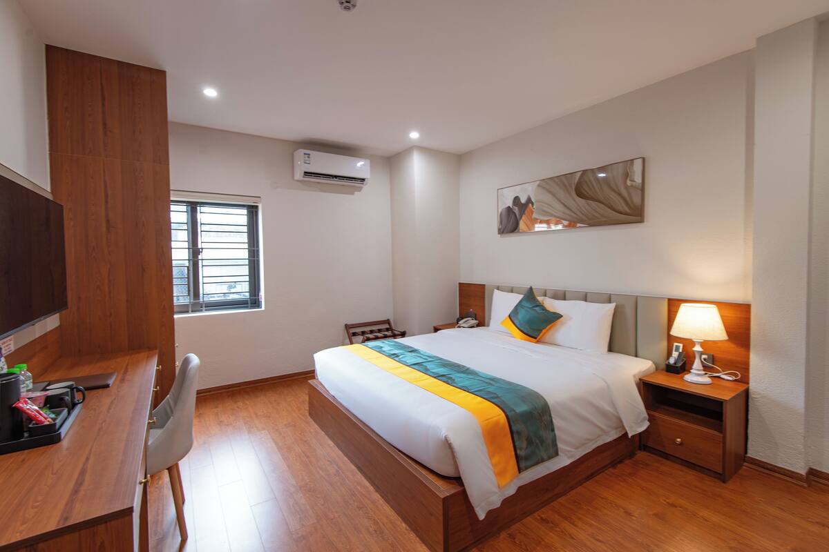 A hotel room with a bed, bedside table, desk, chair, and a window.