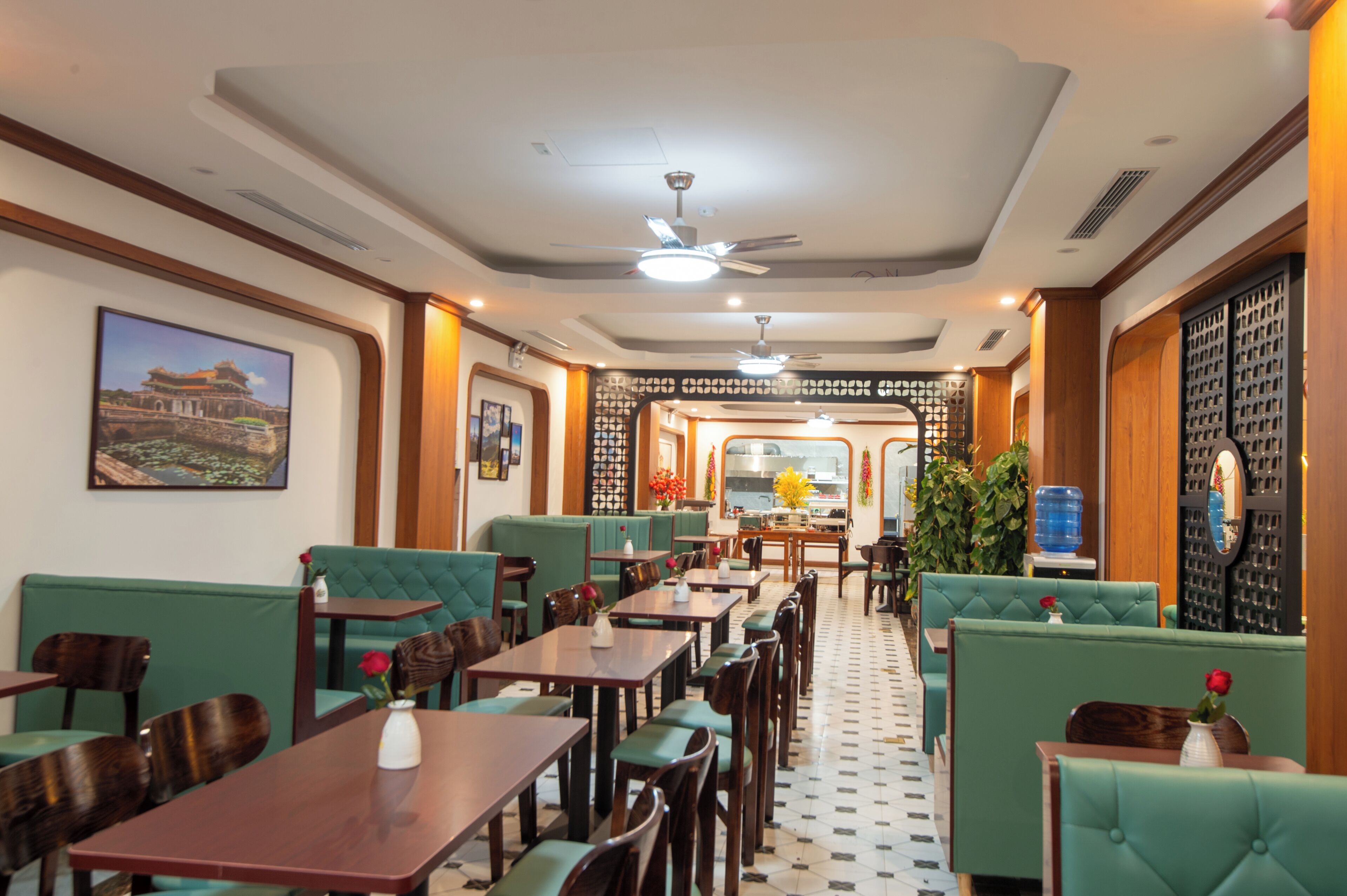 A restaurant with green upholstered booths and wooden tables, a tiled floor, and a ceiling fan.