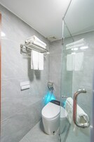 Un baño moderno con cabina de ducha de vidrio, inodoro y toallero con toallas dobladas.