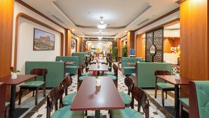 A restaurant with green booths and wooden tables, a tiled floor, and a ceiling fan.