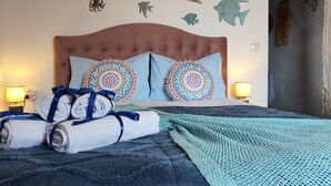 Una cama bien hecha con un edredón azul, dos almohadas decorativas y toallas dobladas.