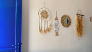 Una habitación con una puerta azul, un sofá a rayas con varios cojines, y adornos en la pared que incluyen un atrapasueños, un farol y un espejo.