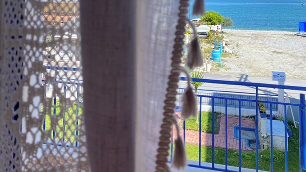 Vista a través de un cortinaje de encaje, con una barandilla azul y un cartel que dice "MANIA MIA" en primer plano.