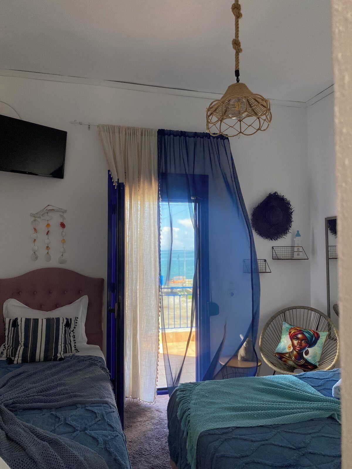 Une chambre avec deux lits, une télévision, une vue sur la mer et un luminaire suspendu.