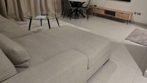 Una sala de estar moderna con un sofá beige grande, una mesa de centro de vidrio, una mesa de comedor con sillas y un aparador de madera.