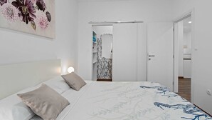 A bedroom with a bed, a nightstand, a wall-mounted lamp, and a door leading to a bathroom.