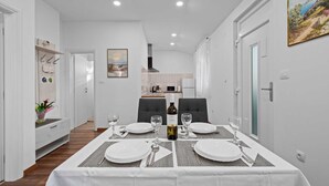 A dining area with a table set for four, a bottle of wine, and a painting on the wall.