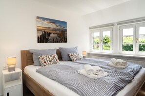 A hotel room with a bed, two bedside tables, a window with a view, and a painting on the wall. - Nala's Hüs - Beautiful house for 6 people with a terrace, parking, and Wi-Fi. (Westerland)