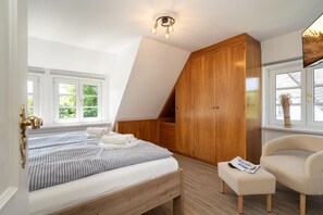 A bedroom with a bed, a wooden wardrobe, a chair, and a window.
