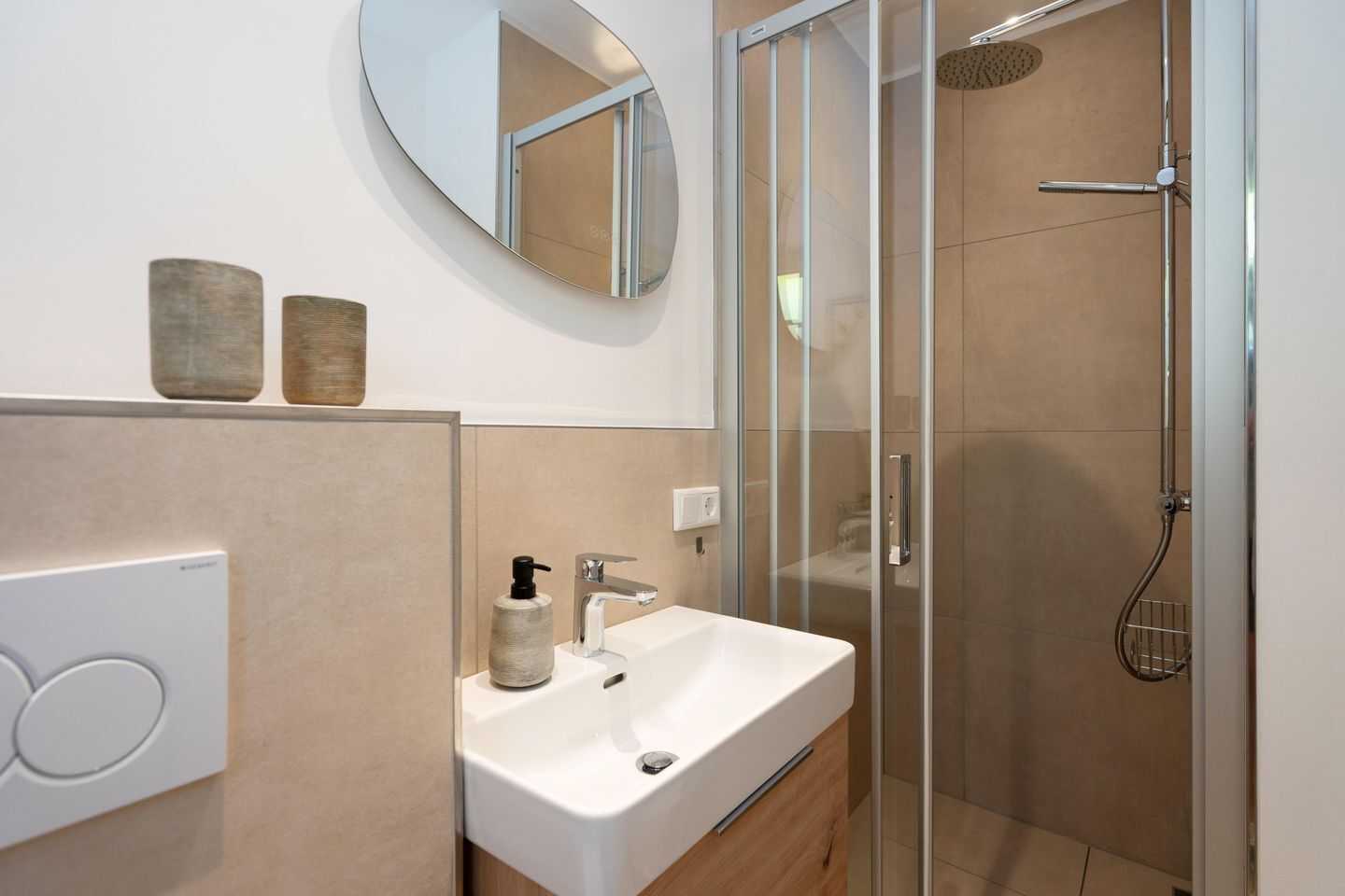 A modern bathroom with a glass-enclosed shower, a white sink, and a round mirror.