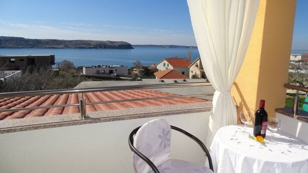Una terraza con una mesa lista para dos, con vistas a un cuerpo de agua y una costa distante.