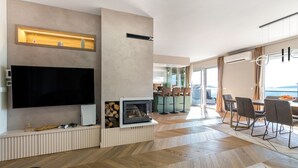 Un salon moderne doté d’un téléviseur à écran plat, d’une cheminée intégrée et d’un coin repas offrant une vue sur la mer.