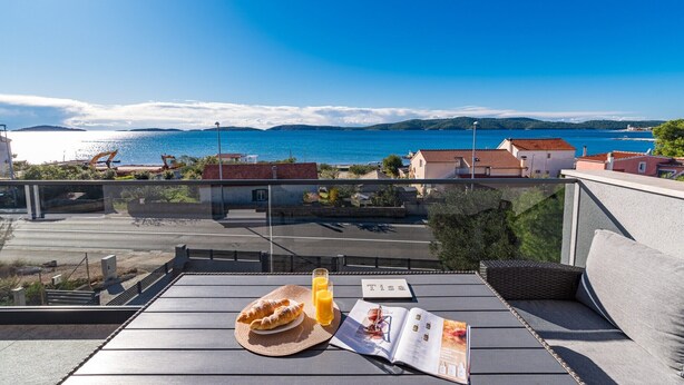 Une terrasse avec vue sur la mer, une table garnie de nourriture et un magazine, et une balustrade en verre.