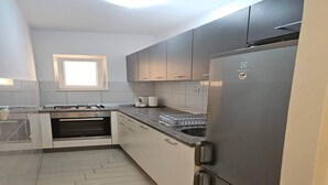 Een moderne keuken met grijze kastjes, een roestvrijstalen koelkast, een inbouwoven en een raam boven de gootsteen.