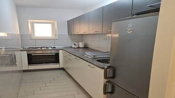 Una cuina moderna amb armaris grisos, un refrigerador d'acer inoxidable, un forn de sobre i una finestra sobre l'aigüera.