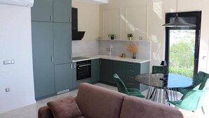 Une cuisine moderne avec des meubles gris, un four noir et une table ronde en verre entourée de chaises vertes.