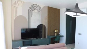 Un salon moderne avec un grand téléviseur à écran plat, un meuble de rangement turquoise et un fauteuil vert.
