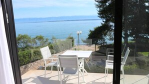 Un balcon avec une table et des chaises, donnant sur une étendue d’eau et une zone verdoyante.