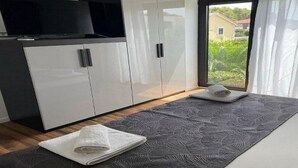 Ein modernes Zimmer mit großem Kleiderschrank, Flachbildfernseher und Blick auf Grün durch ein großes Fenster.