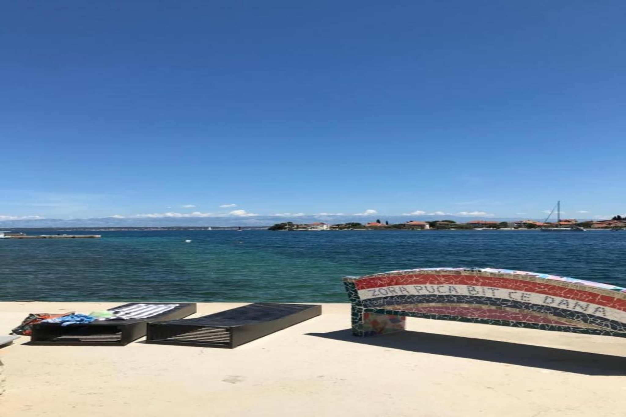 A beach with a bench and a sign reading "ZORA PUCA BITE CE DANA" in the foreground.