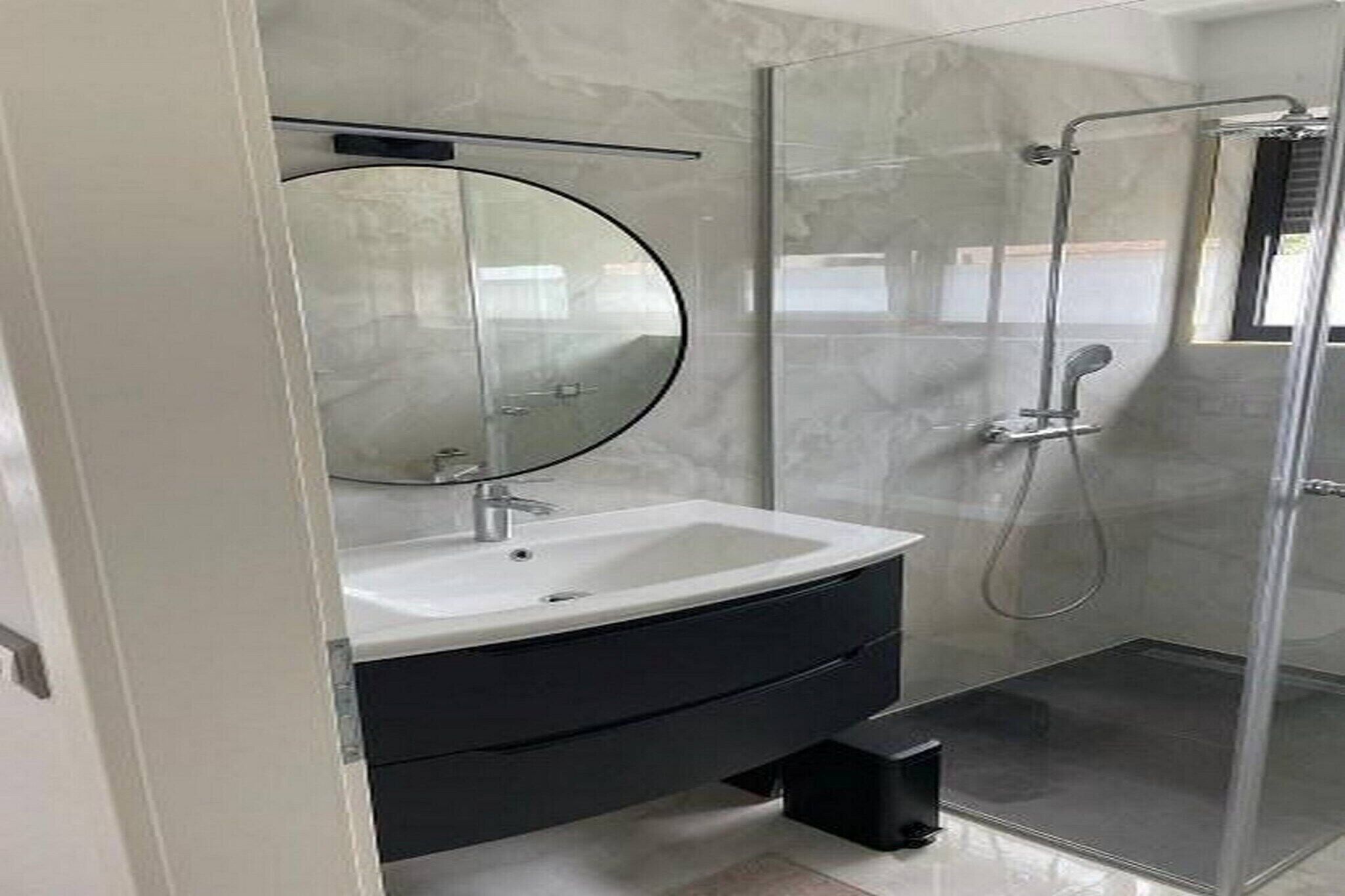 Ein modernes Badezimmer mit einem weißen Waschbecken, einem schwarzen Waschtisch und einer Duschkabine aus Glas.