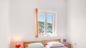 A bedroom with two beds, a window with curtains, and a nightstand with a lamp.