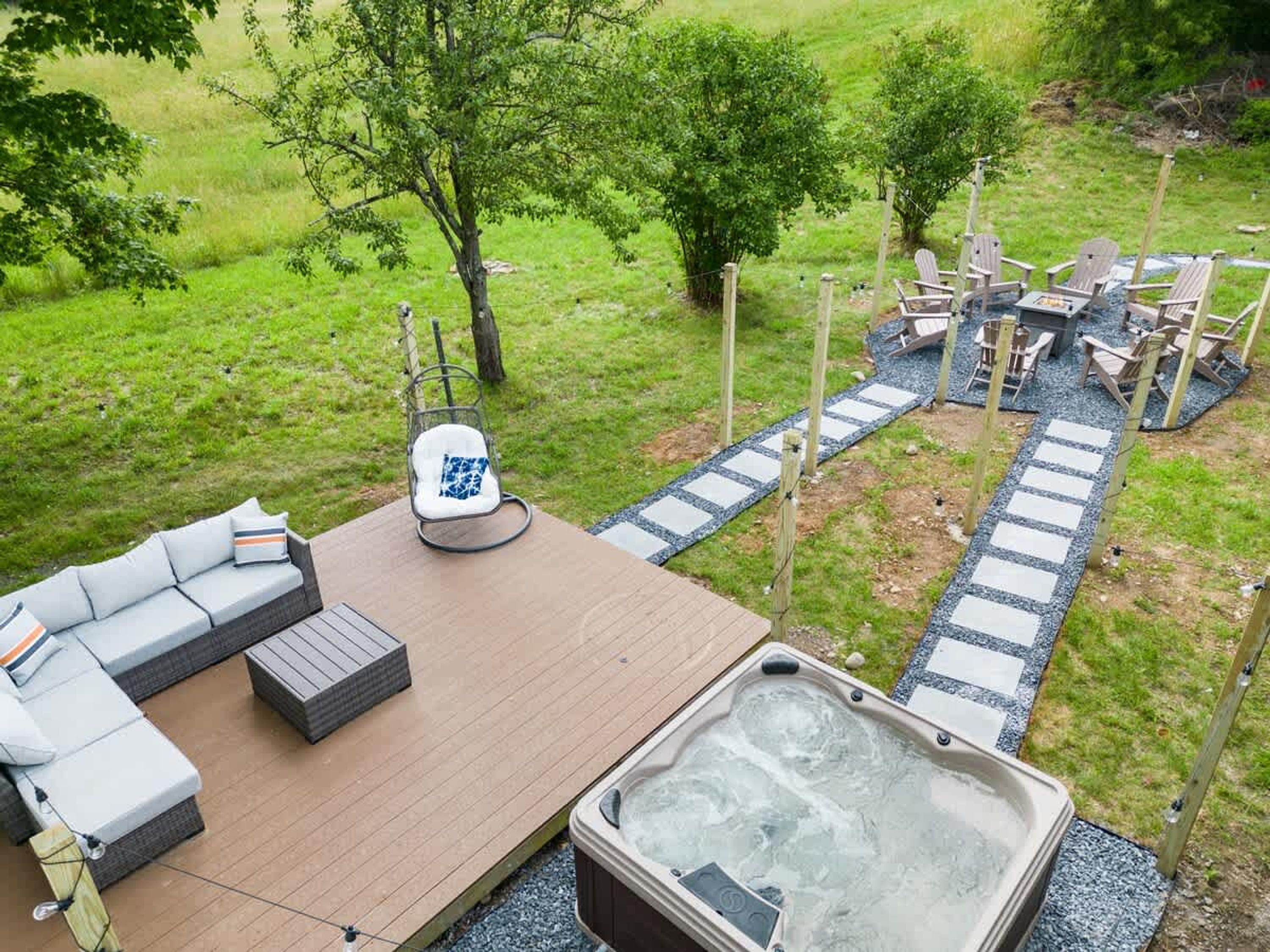 A hot tub with a wooden deck, outdoor seating, and a stone pathway.