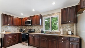A modern kitchen with dark wood cabinets, a stainless steel stove, and a large window providing natural light.