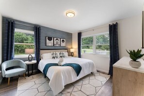 A modern hotel room with a large bed, a small desk, a chair, and a view of the outdoors. - Charming Poconos Retreat w spa Fire pit Deck (East Stroudsburg)