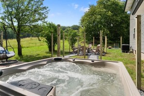 Un jacuzzi con cubierta de madera y sillas, rodeado de césped y árboles.