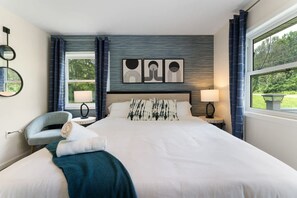 A modern bedroom with a large bed, two bedside tables, a chair, and artwork on the wall. - Charming Poconos Retreat w spa Fire pit Deck (East Stroudsburg)