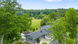 A house with a grey roof and white trim, surrounded by lush green trees and a grassy field.