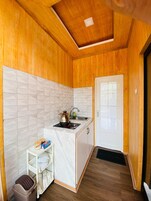 Una cocina compacta con paredes de madera, salpicadero blanco de azulejos, un lavamanos, una estufa y un estante pequeño con utensilios de cocina.