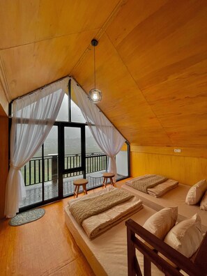 Quarto de cabana de madeira aconchegante, com uma janela grande, duas camas, uma mesa pequena e um lustre.