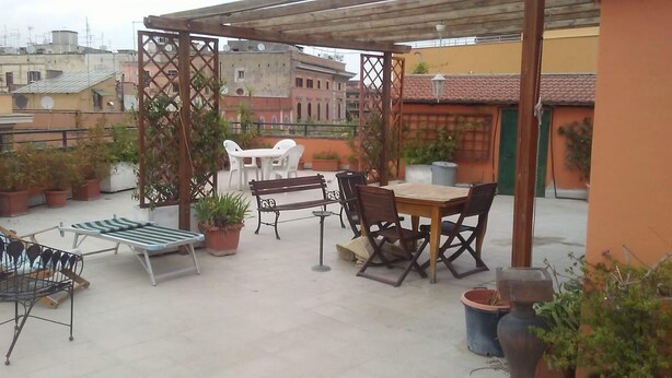 An outdoor patio area with a wooden table and chairs, a bench, and potted plants.