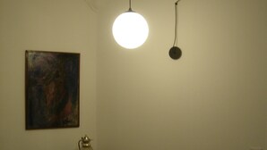 A dining area with a round table, white chairs, a painting on the wall, and a hanging light fixture.