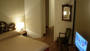 A hotel room with a bed, a chair, a television, and a door leading to another room.