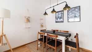 Un coin repas avec une table blanche, des chaises en bois et des coussins noirs. Trois lampes suspendues sont placées au-dessus de la table.