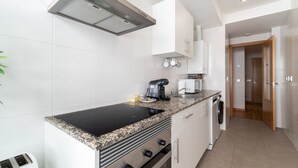 Une cuisine moderne avec des meubles blancs, une plaque de cuisson à induction noire, un four encastré, une machine à café et un four à micro-ondes.