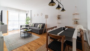 Un salon moderne comprenant un canapé, une table basse, une table à manger et des chaises. On y trouve également des étagères décoratives fixées au mur et un lampadaire.