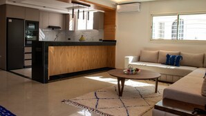 A modern kitchen with a wooden island, a built-in oven, and a dining area with a round table and sofa. - ZAYANE HOMES RABAT BEACH (Harhoura)