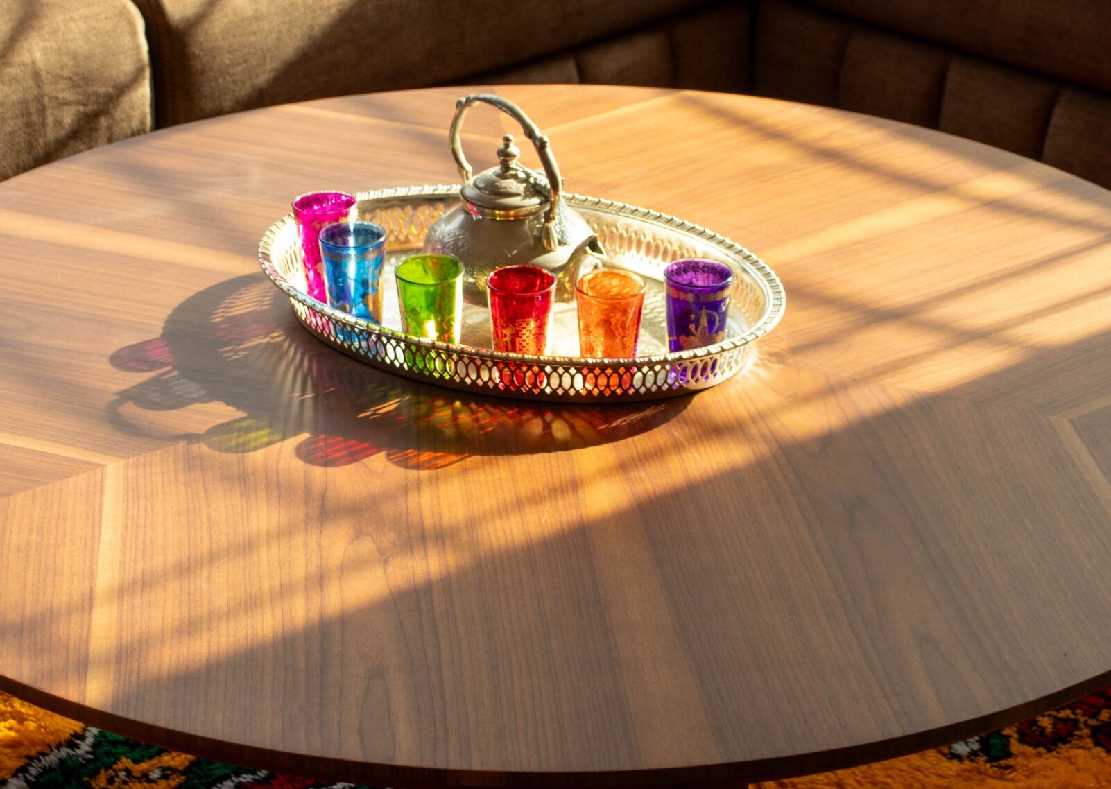Een ronde houten tafel met een metalen dienblad waarop kleurrijke glazen en een theepot staan.