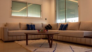 A living room with a beige sofa, a wooden coffee table, and a patterned rug. - ZAYANE HOMES RABAT BEACH (Harhoura)