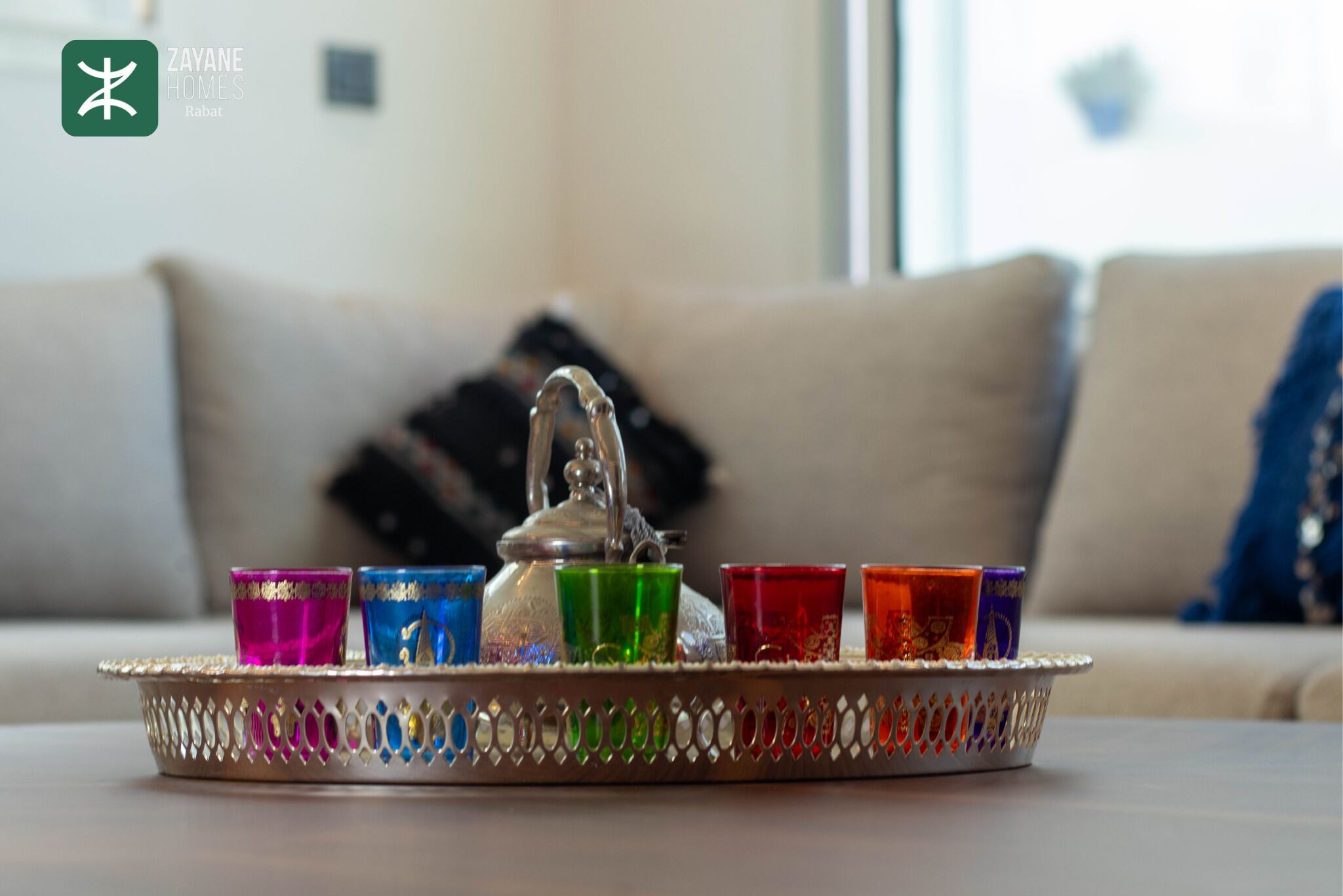 Uma bandeja com copos coloridos e uma chaleira sobre uma mesa em uma sala de estar.