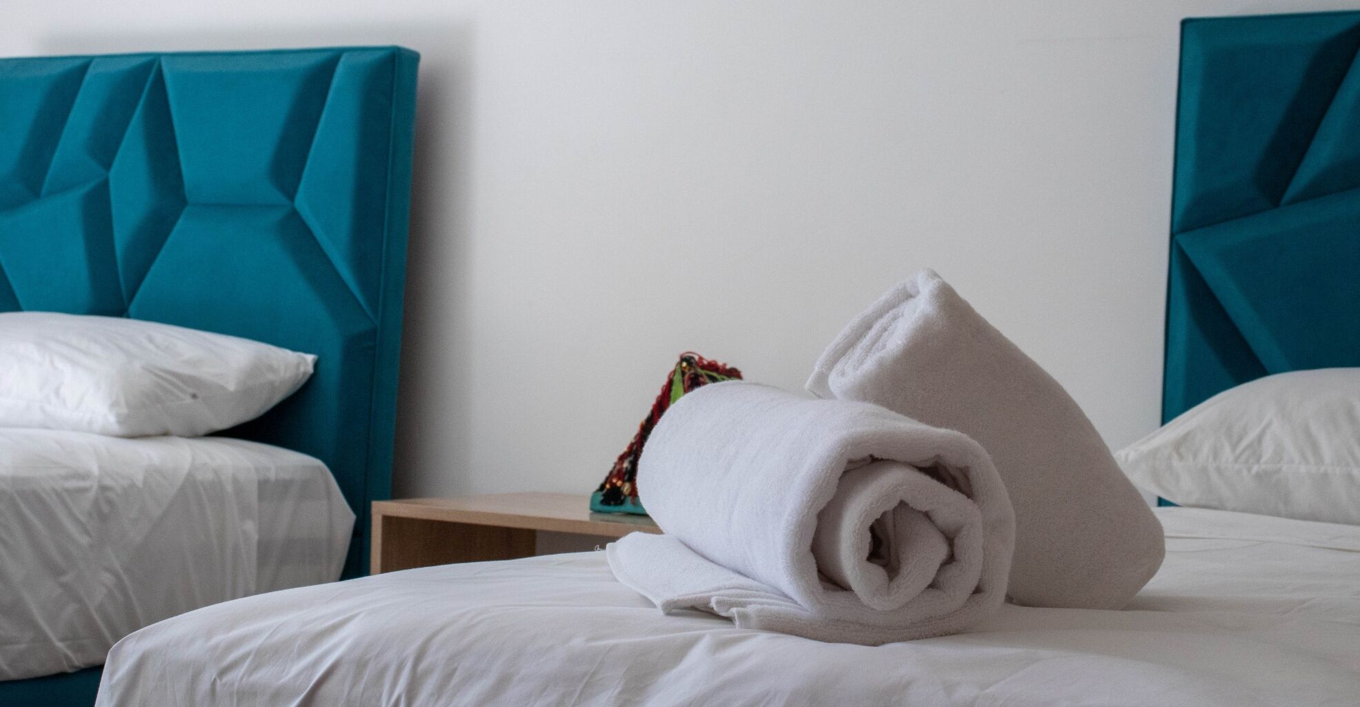 A hotel room with two beds, each with teal headboards and white bedding.