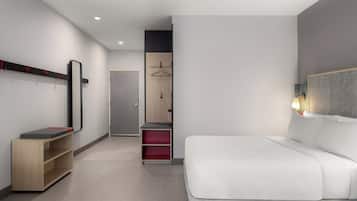 Una habitación de hotel moderna con una cama grande, un armario, un espejo y un pequeño escritorio con una silla.