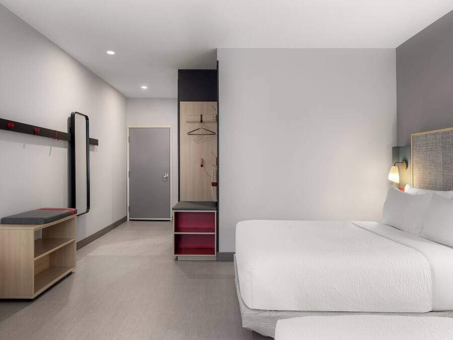 Una habitación de hotel moderna con una cama grande, un armario, un espejo y un pequeño escritorio con una silla.
