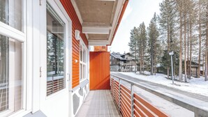 A covered outdoor balcony with a wooden railing, a snow-covered ground, and a view of a residential area with tall trees and houses. - 3BR Holiday Apt. with Sauna (Kittilä)